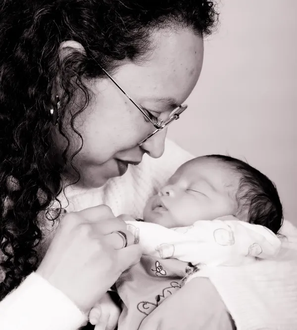 A mother kissing her newborn baby in a black and white portrait